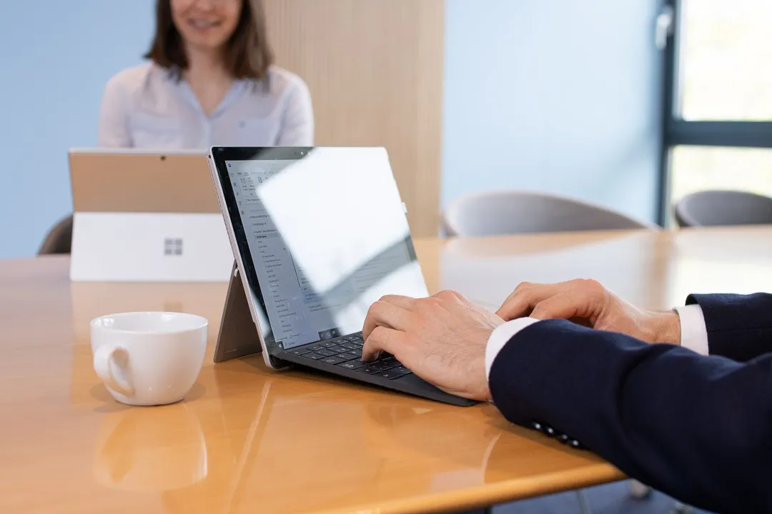 Hände auf der Tastatur eines Laptops an einem Besprechungstisch
