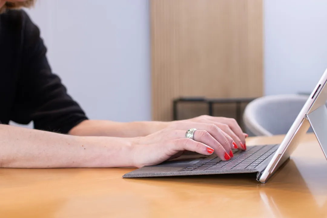 Hände tippen auf der Tastatur eines Tablets an einem Holztisch