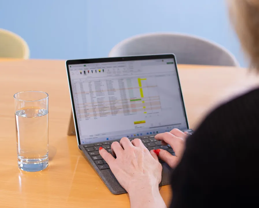 Hände tippen auf einem Laptop mit geöffneter Tabelle, daneben ein Glas Wasser