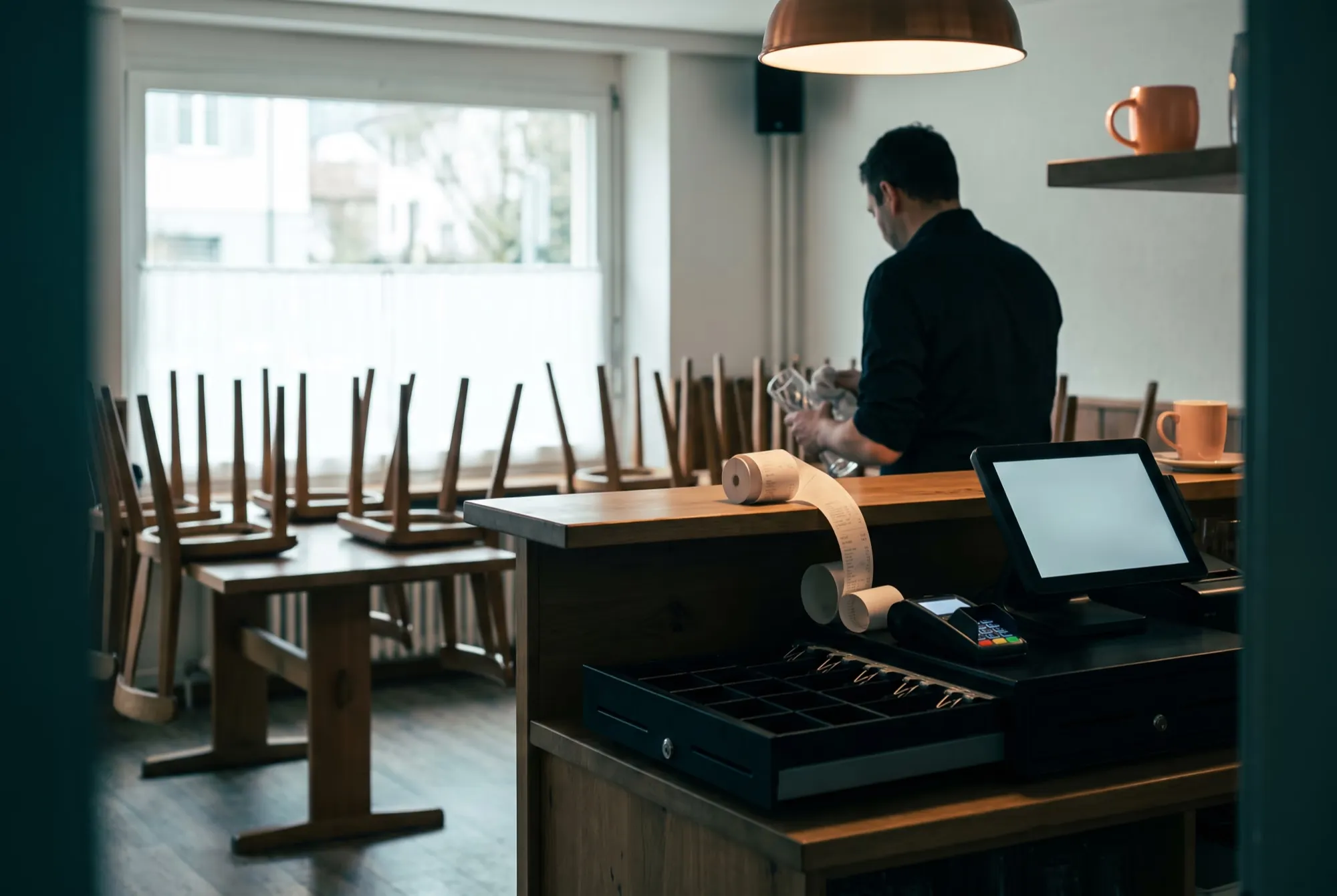 Bar nach Feierabend mit hochgestellten Stühlen, offener Kassenschublade, Kartenterminal und Belegrolle