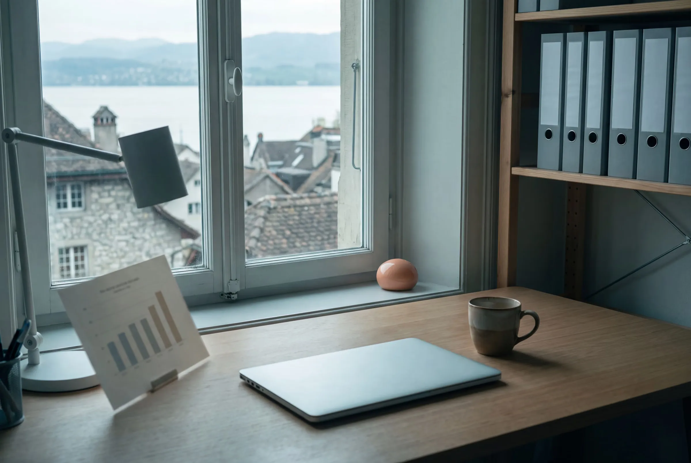 Aufgeräumter Arbeitsplatz mit Laptop und Monatsübersicht, draussen Altstadt und See