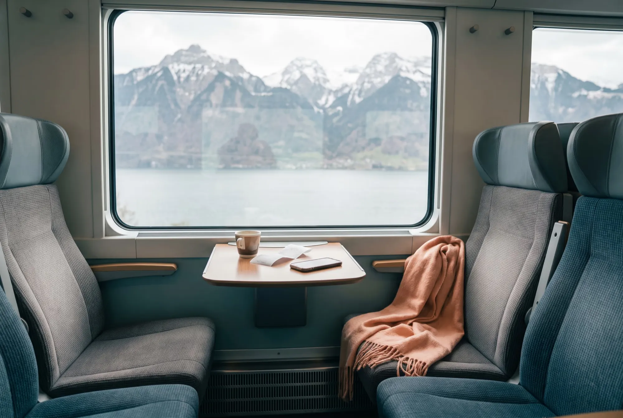 Zugabteil am Fenster mit Klapptisch, Kaffee, Quittung und Smartphone, draussen See und Berge